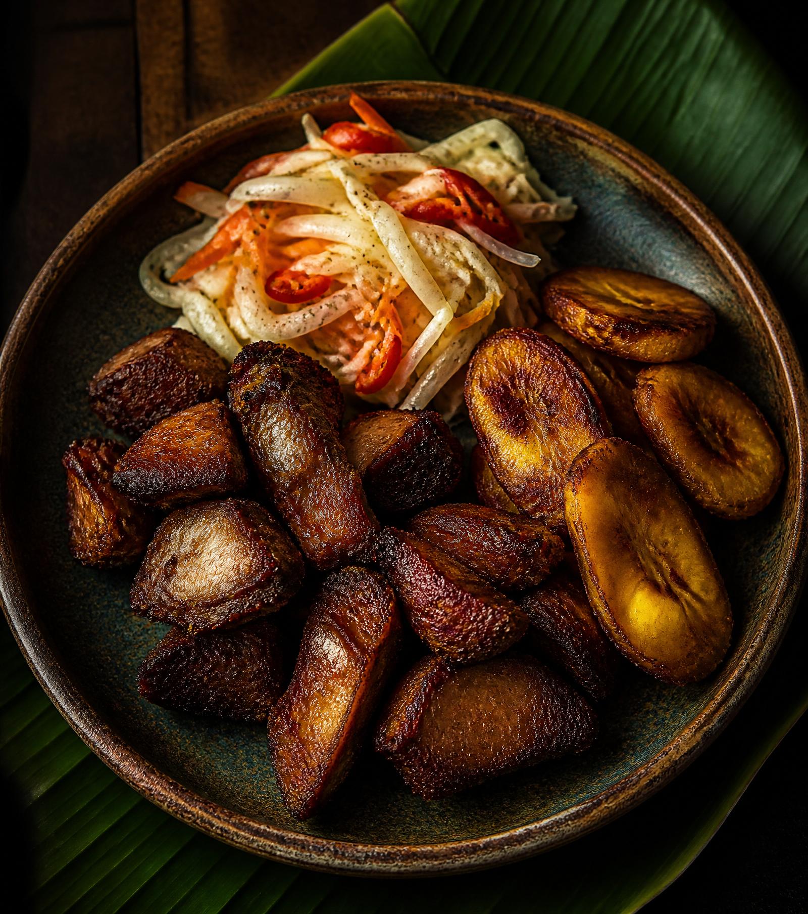 Griyo — Haitian fried pork with pikliz and plantains on a rustic ceramic plate